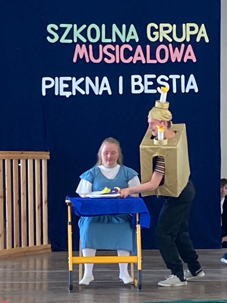 Na scenie w auli szkolnej uczeń przebrany za postać Pana Płomyka oraz uczennica w roli Belli z  musicalu "Piękna i Bestia"