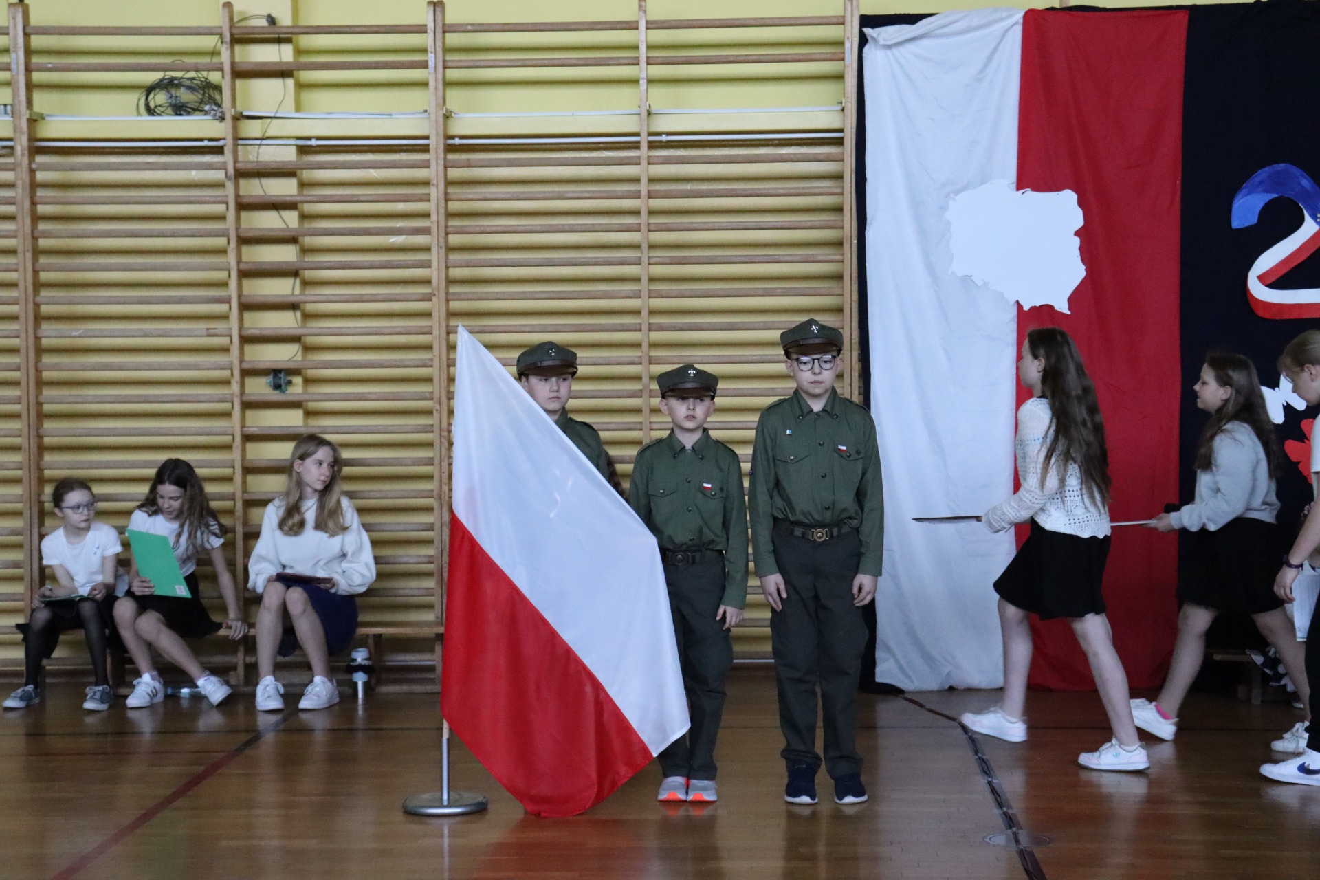 Trzech harcerzy stoi i trzyma flagę Polski.