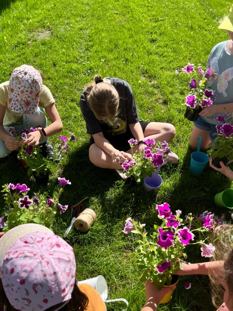 Dzieci siedzące na trawie, trzymające kwiaty doniczkowe w ręce.