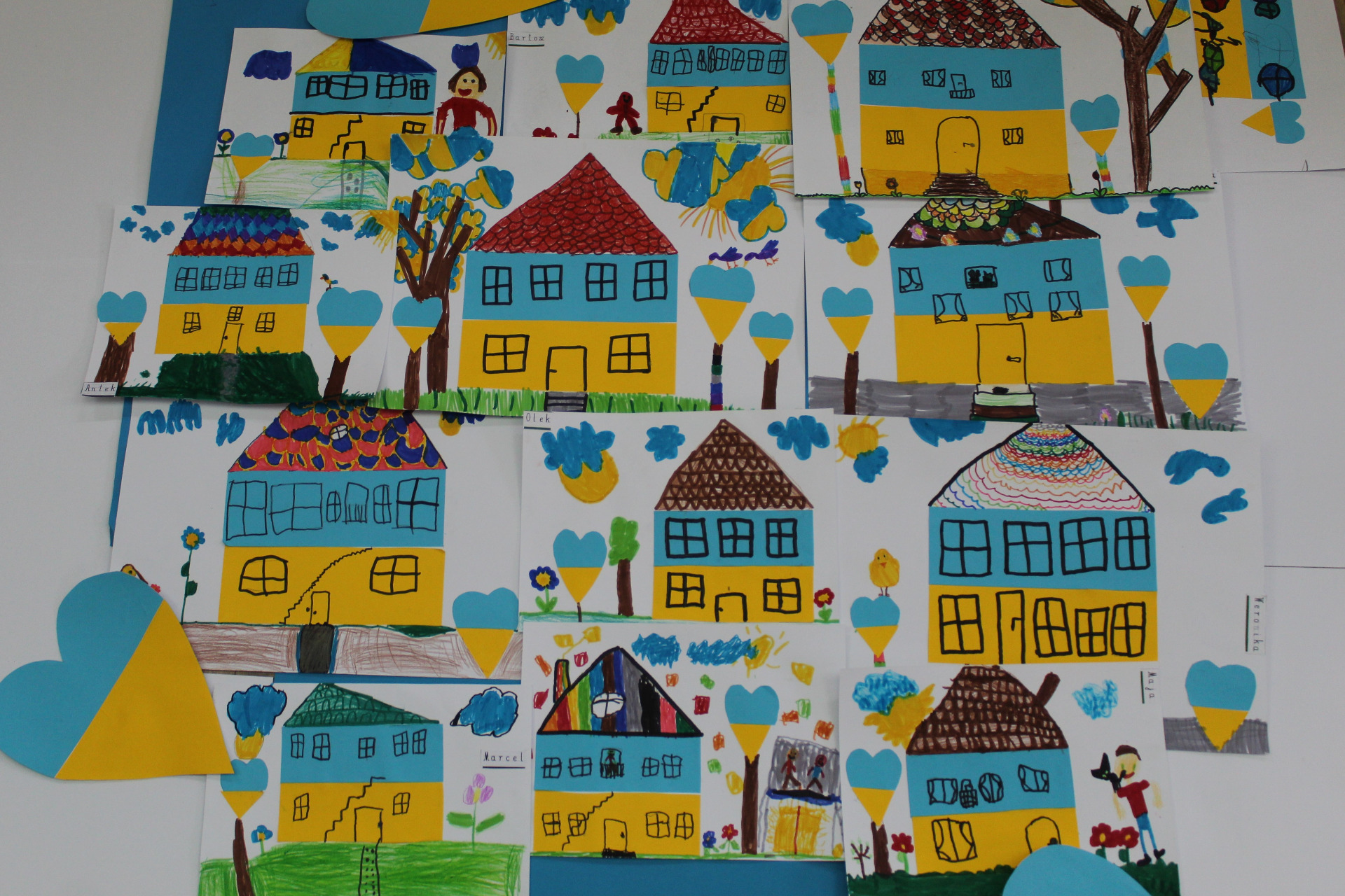 Zbiór prac plastycznych wykonanych przez dzieci, który przedstawia domy w barwach flagi Ukrainy.