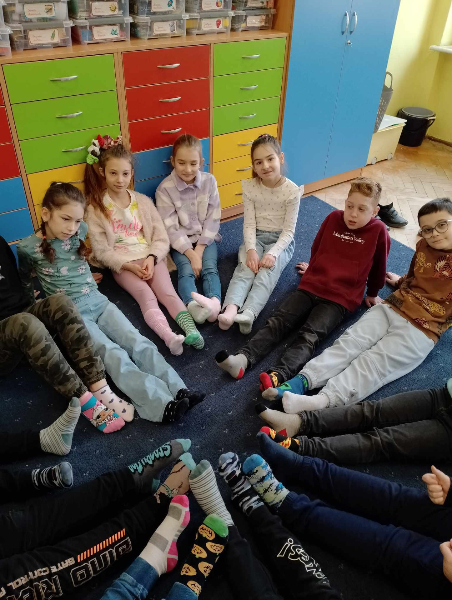 Dzień Kolorowej Skarpetki. Dzieci z klasy 3c siedzą w kręgu, prezentują swoje kolorowe skarpetki.