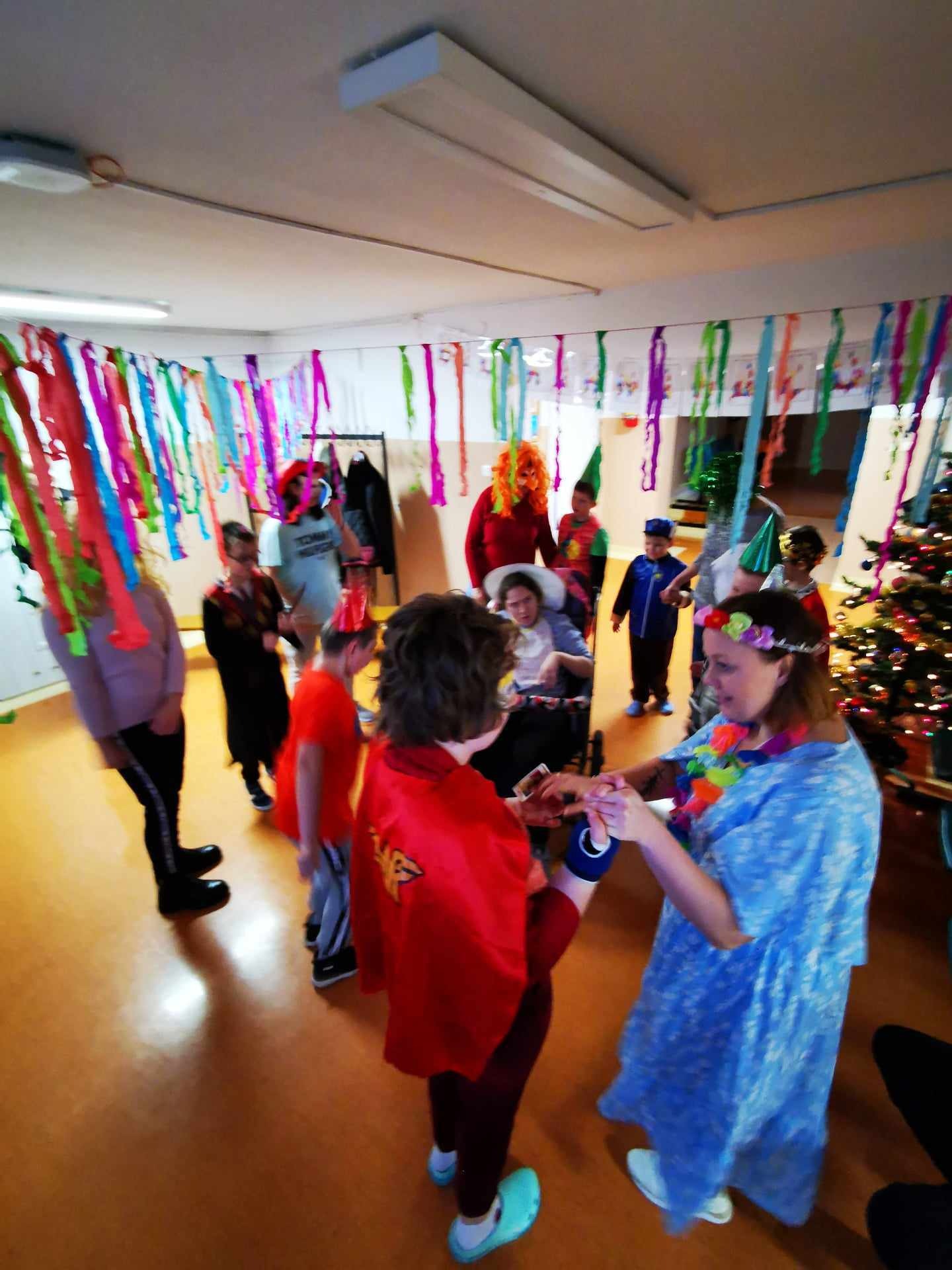Uczniowie wraz z nauczycielami tańczą w kolorowych strojach.