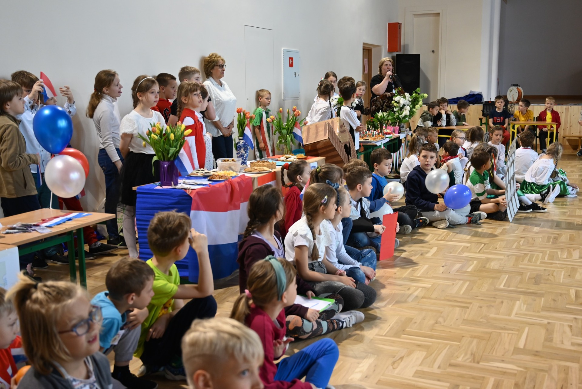 Duża grupa dzieci z nauczycielkami przy stoiskach prezentujących wybrane państwo europejskie