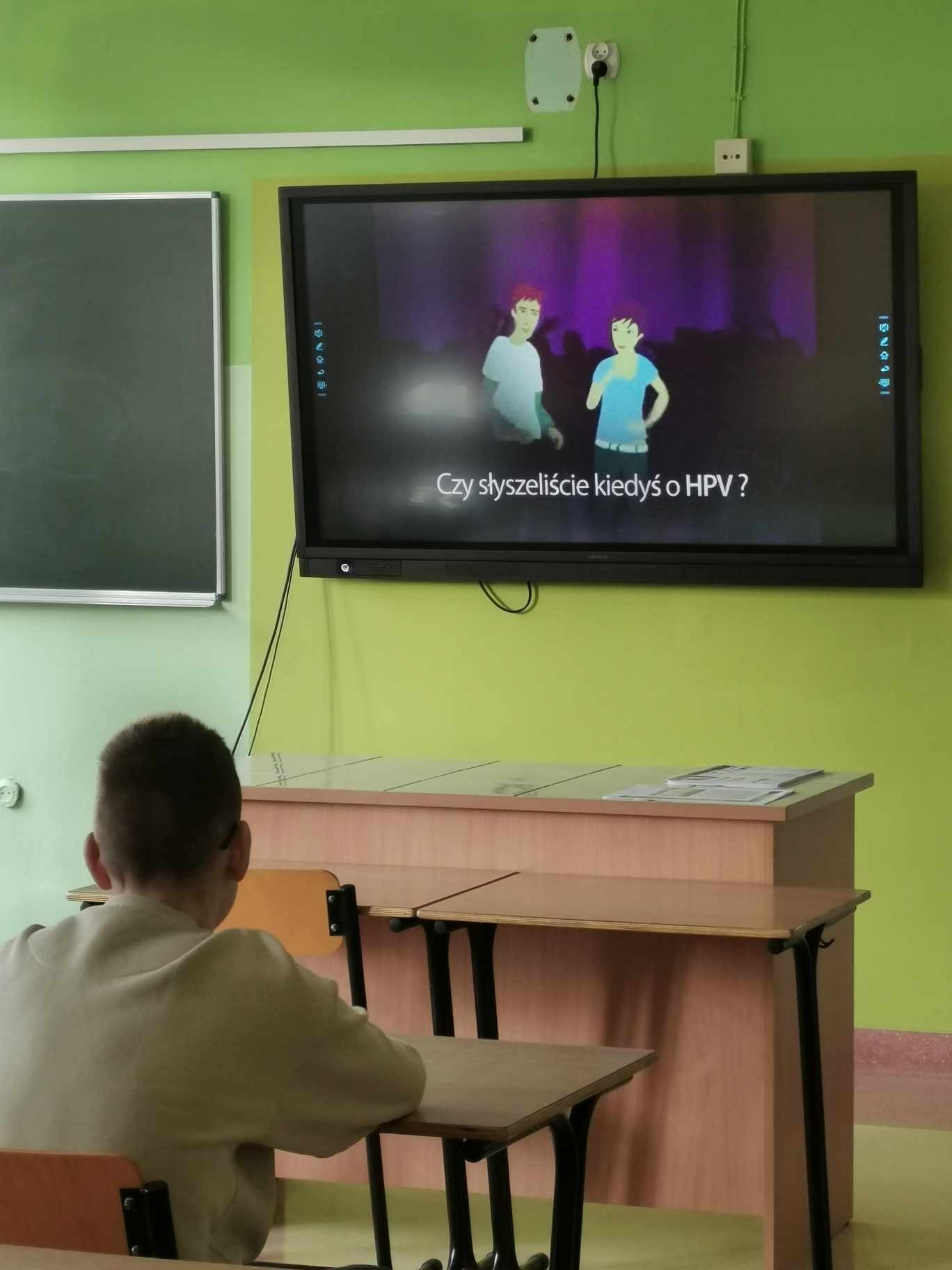 Uczeń  odwrócony od aparatu plecami oglądają prezentację