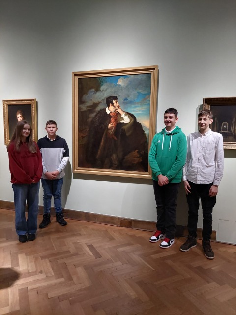 4 uczniów stoi wokół obrazu Adama Mickiewicza.
