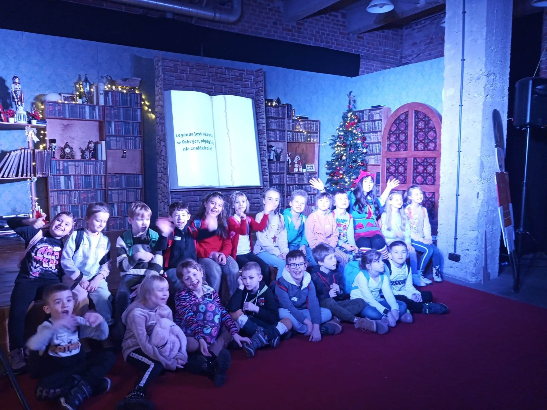Grupa dzieci siedzi na scenie . W tle pokój Elfów i Wielka Księga Legend.