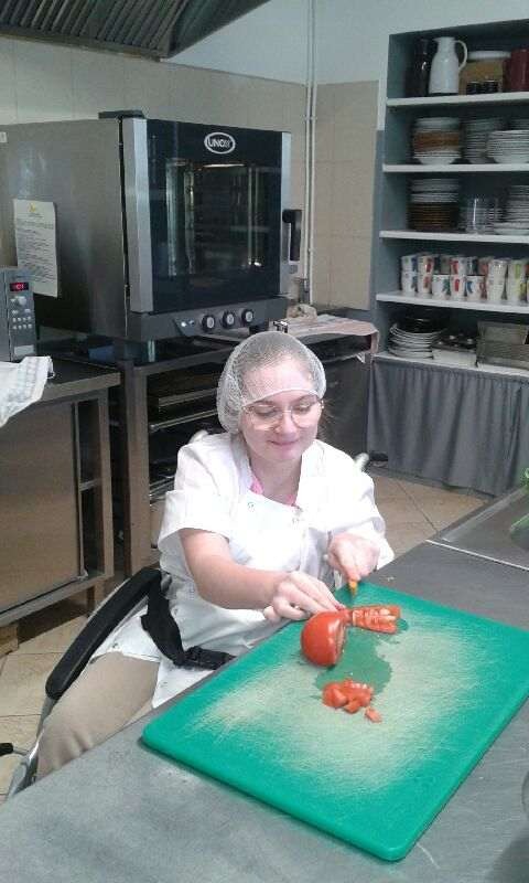 Uczennica na wózku inwalidzkim w białym fartuchu kroi pomidora
